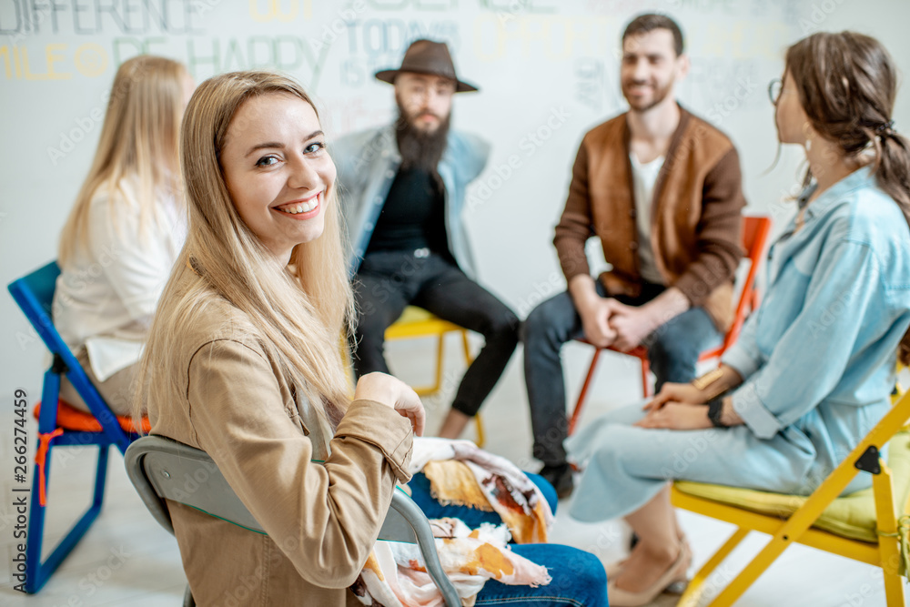 Portrait of a smiling woman sitting in a circle with group of people during the psychological traini