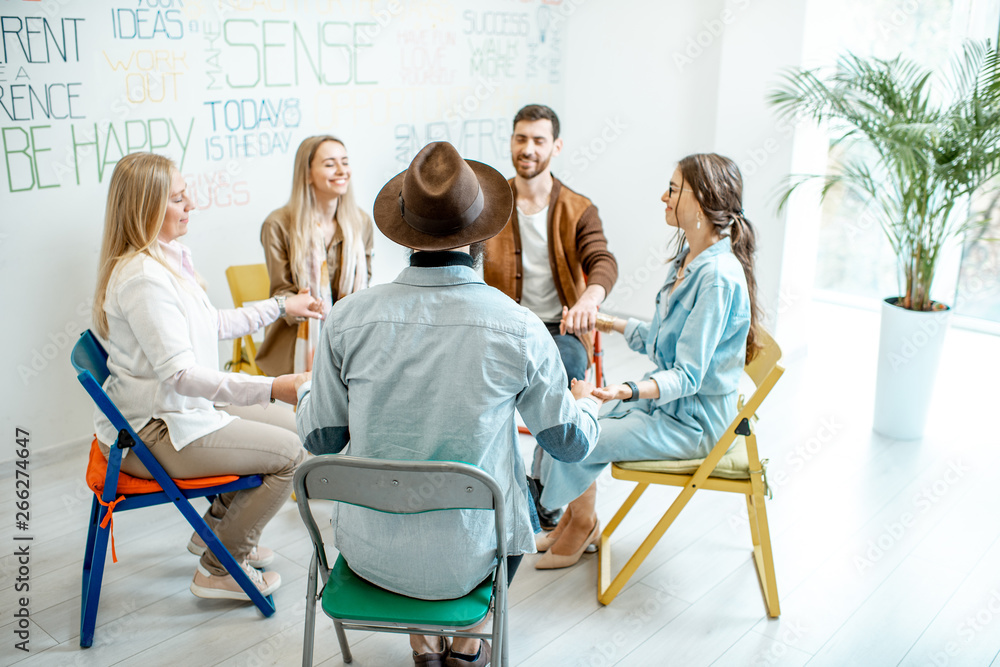 Group of diverse people keeping hands together, sitting in a circle during the psychological therapy