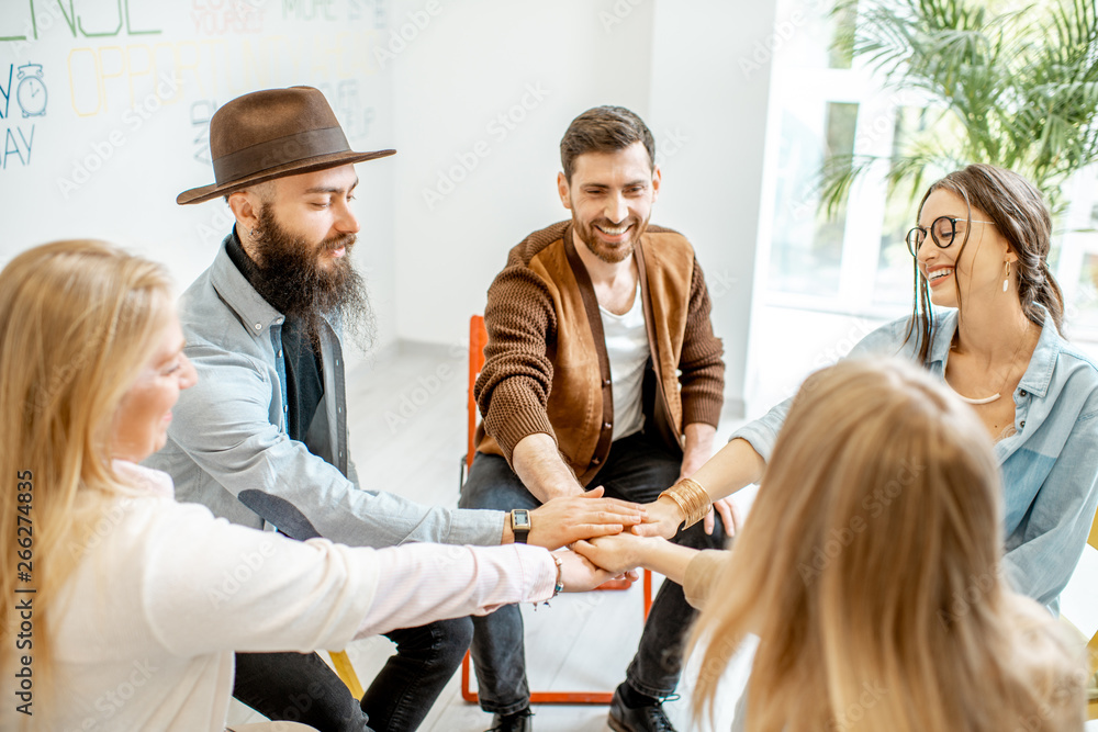 Group of diverse people keeping hands together, sitting in a circle during the psychological therapy