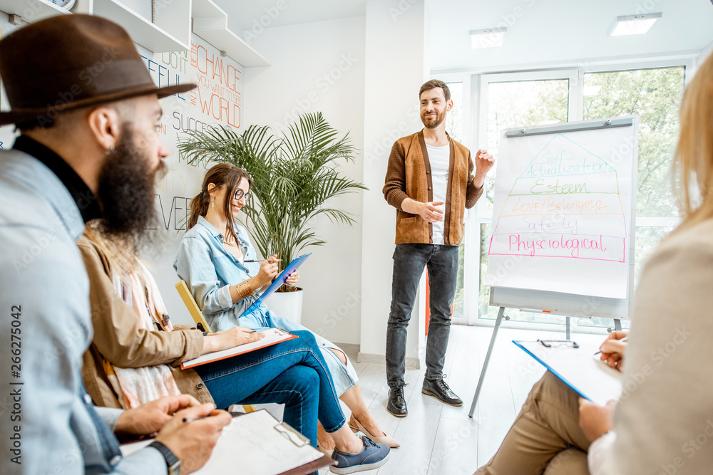 Group of diverse people during the psychological seminar with male coach showing on flipchart in the