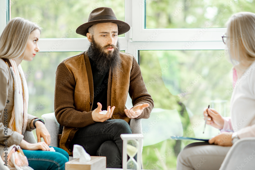 Young couple having misunderstandings during the psychological counseling with senior female psychol