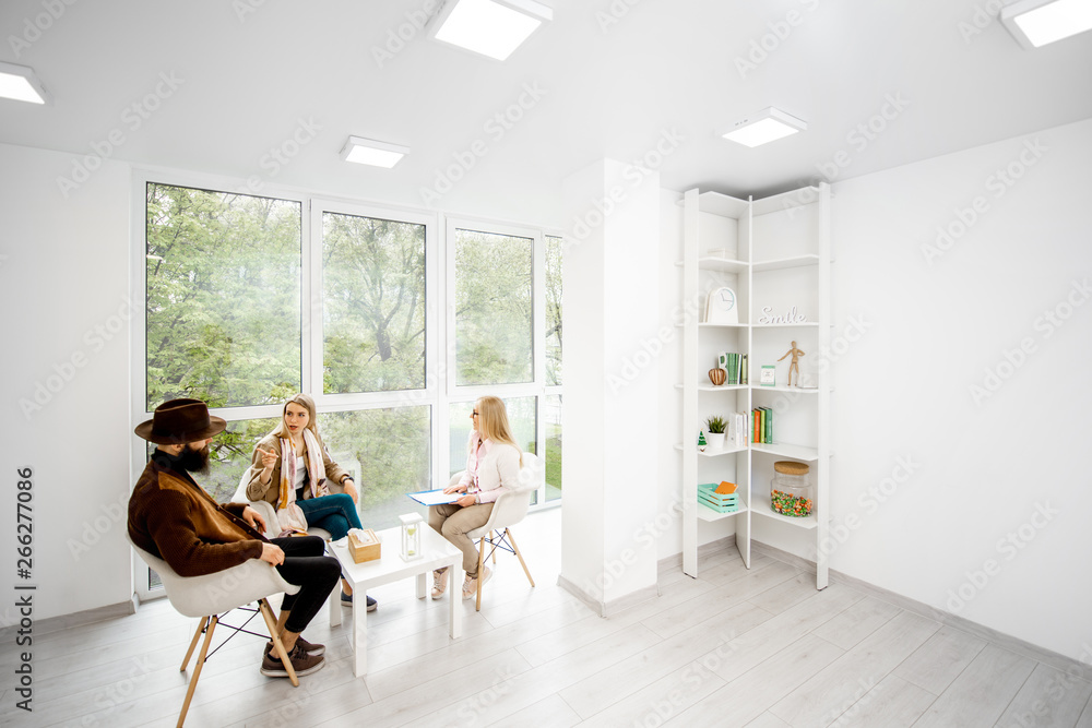 Young couple with psychologist sitting during the mental therapy in the white spacious office. Wide 