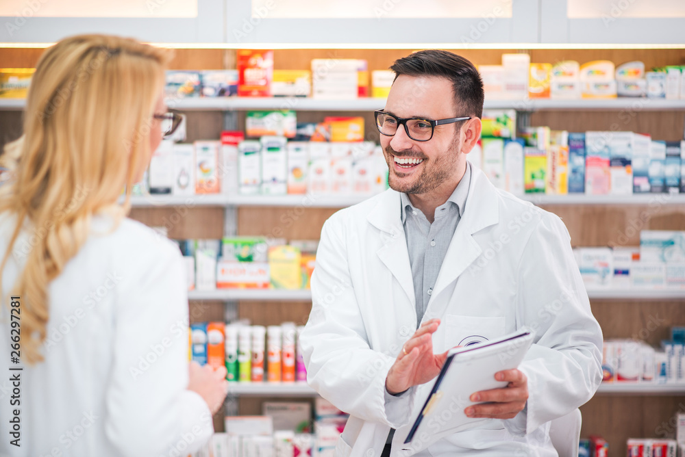 Two cheerful pharmacists working on medicines inventory at hospital pharmacy.