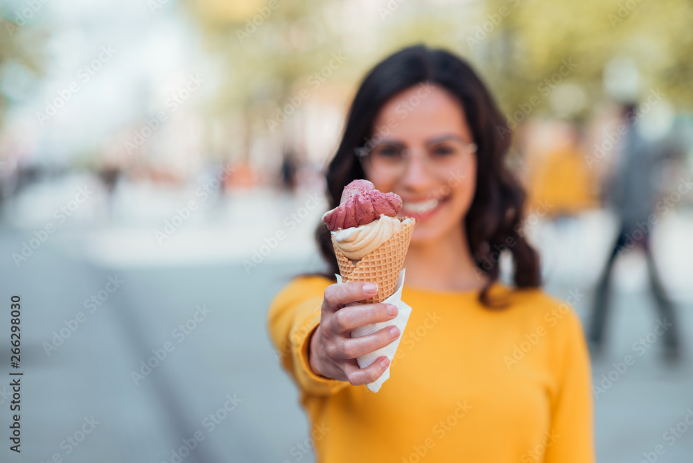 Vacation concept.Young woman offering ice cream toward camera, focus on ice cream.