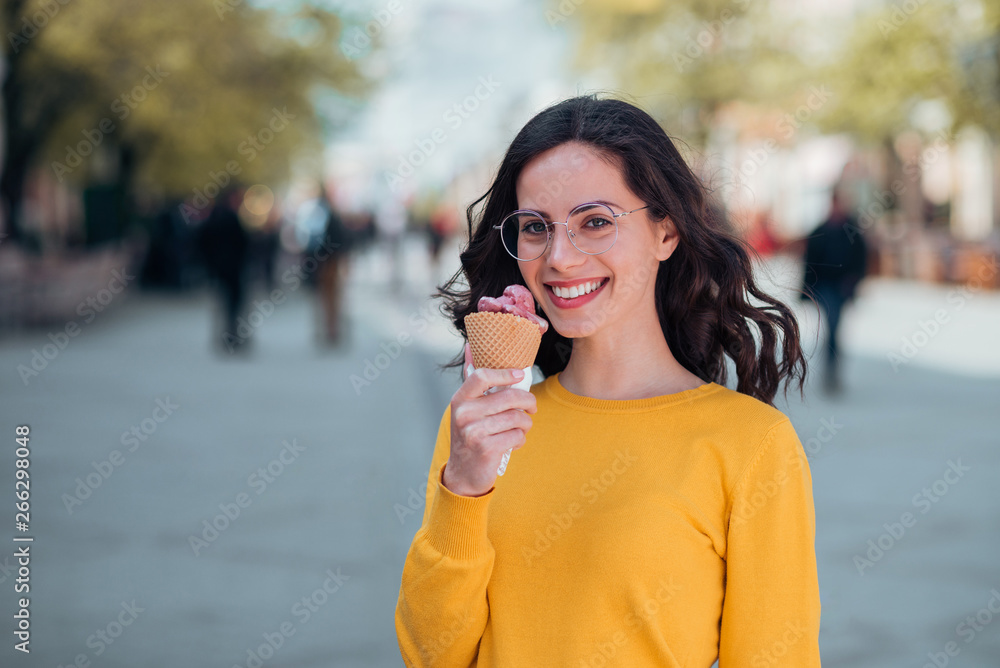 春天，一位面带微笑的年轻女子在镇上的街道上吃冰淇淋。