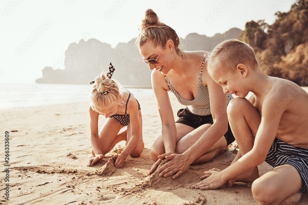 Mother and children playing on a sandy beach during vacation