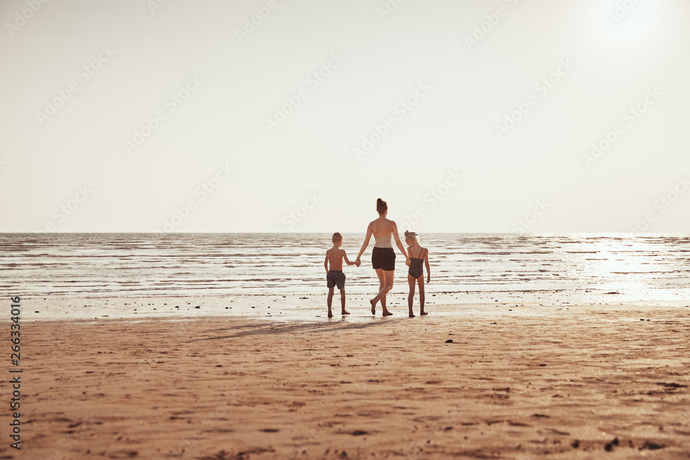 Mother and children holding hands while walking along a beach