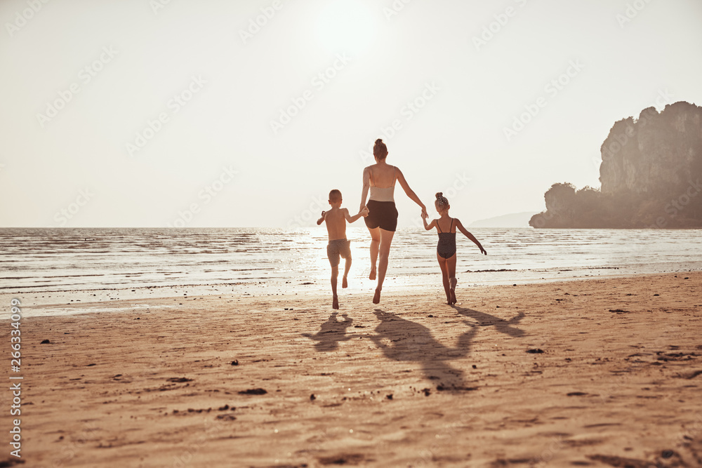 Mother and children holding hands while skipping along a beach