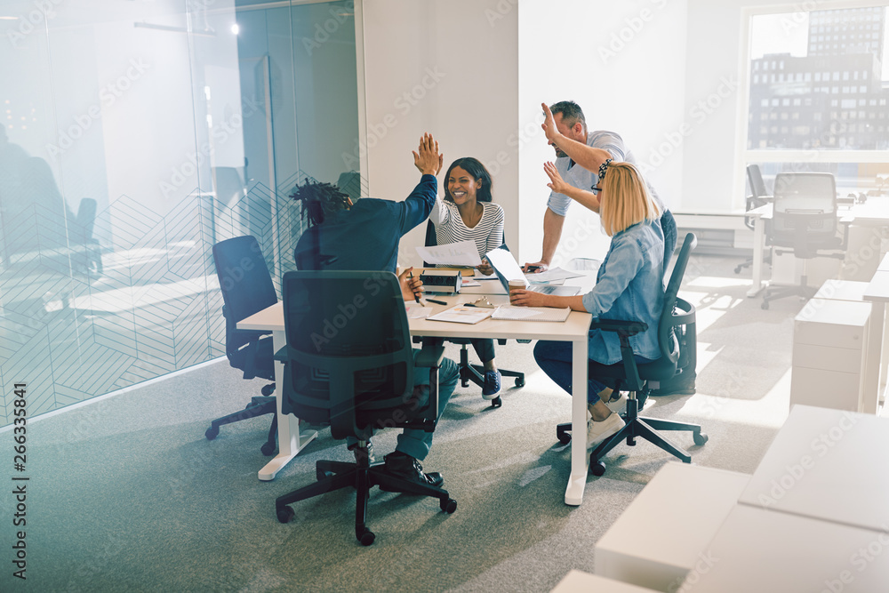 Diverse work colleagues excitedly high fiving during an office m