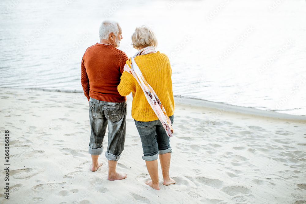 Senior couple dressed in colorful sweaters enjoying nature standing together on the sandy beach near