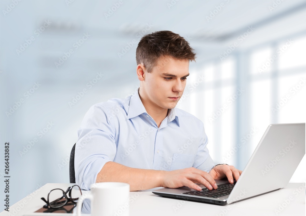 Happy young man works on his laptop with coffee at the table