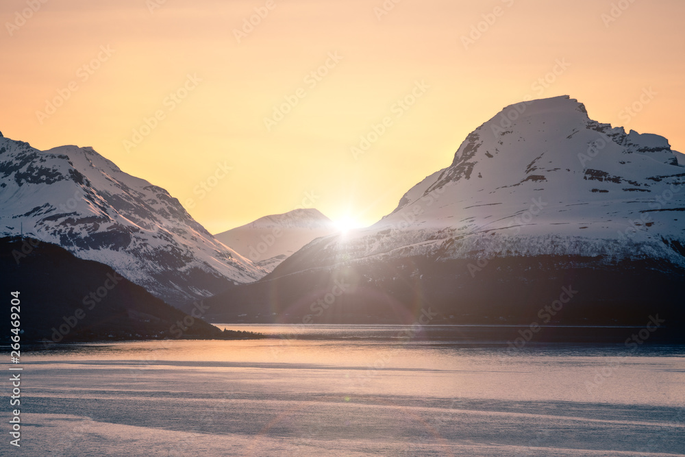 Snow covered mountains and fjord at sunset with lens flare effect