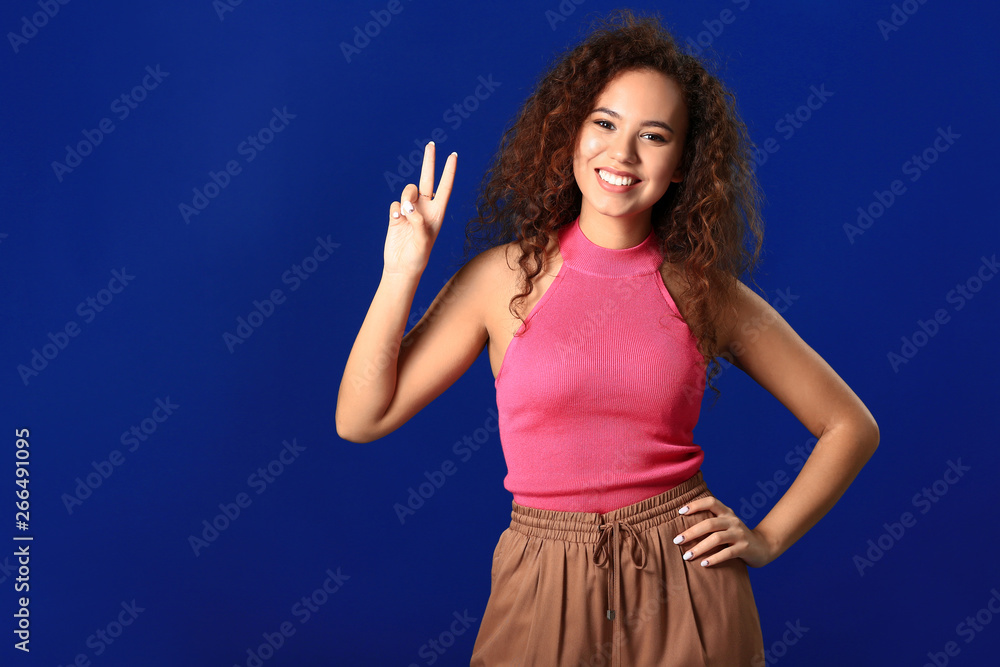 Beautiful young woman showing victory gesture on color background