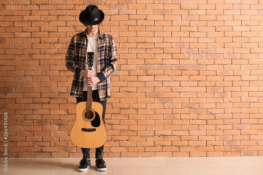 Handsome young man with guitar near brick wall