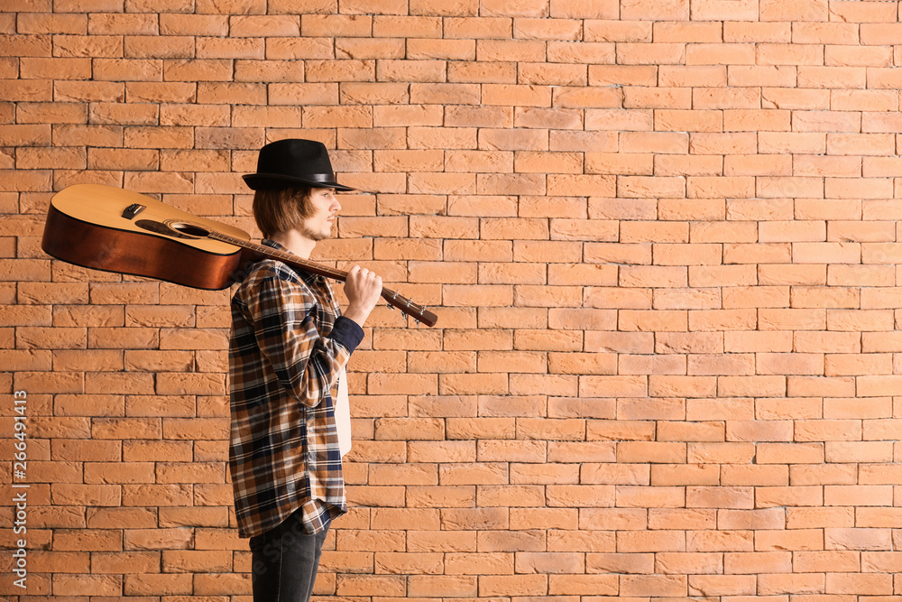 Handsome young man with guitar near brick wall