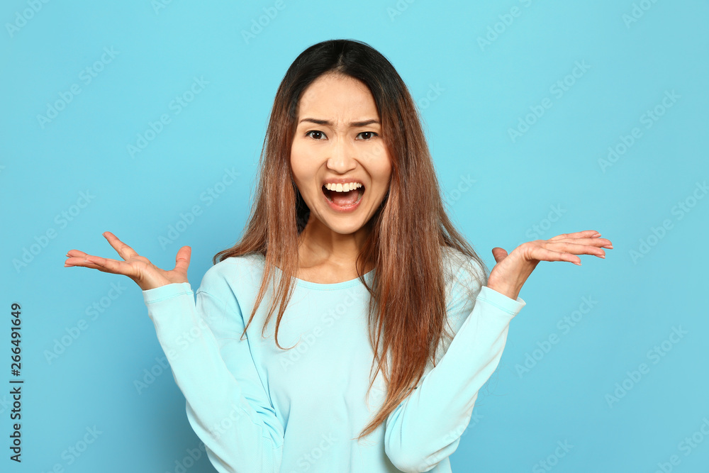 Portrait of angry Asian woman on color background