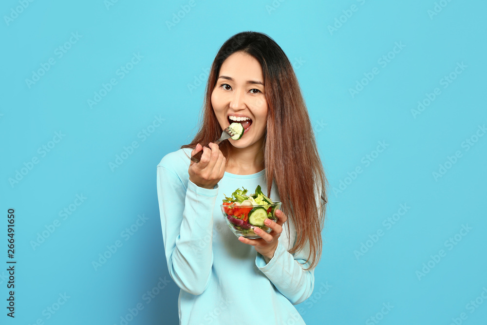 Asian woman with vegetable salad on color background