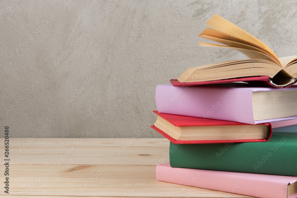 Education and reading concept - group of colorful books on the wooden table, concrete wall blackboar