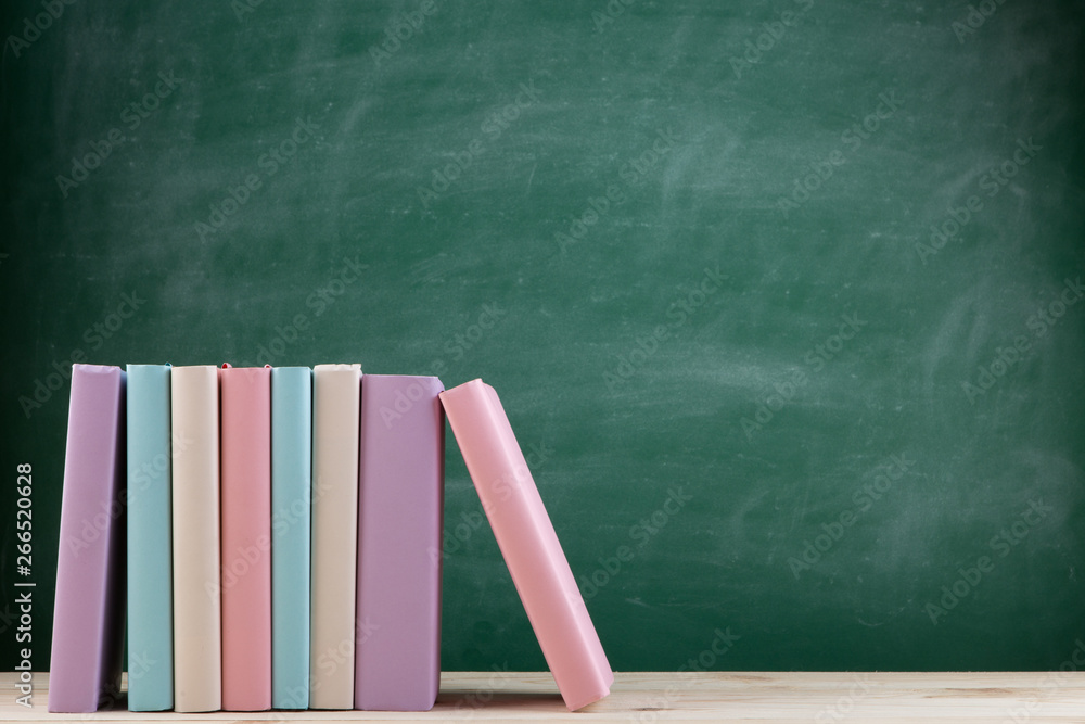 Education and reading concept - group of colorful books on the wooden table in the classroom, blackb