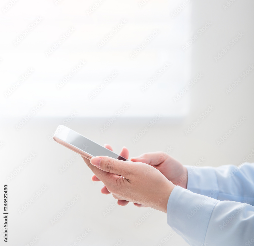 Side view of asia young business woman in blue shirt dress standing beside window and using smart ph