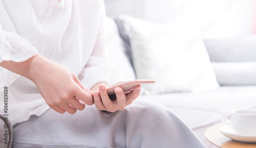 Side view of asia young woman in white sitting on sofa and using smart phone in bright living room, 