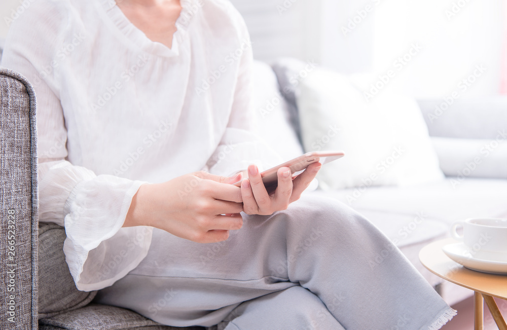 Side view of asia young woman in white sitting on sofa and using smart phone in bright living room, 