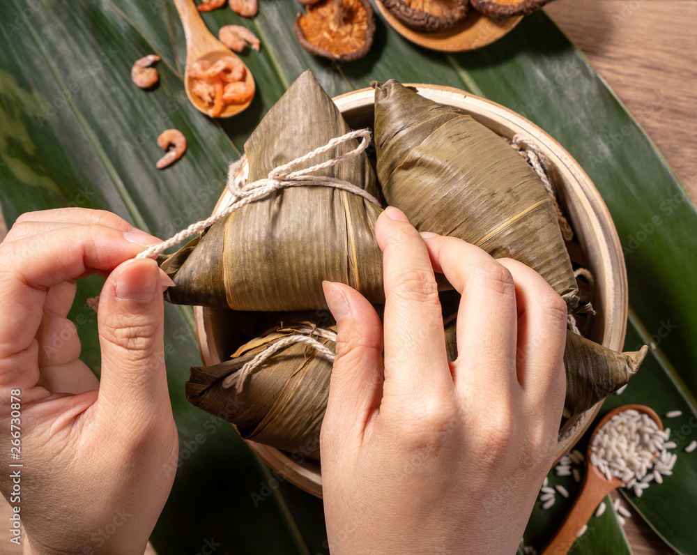 Zongzi, woman eating steamed rice dumplings on wooden table, food in dragon boat festival duanwu con