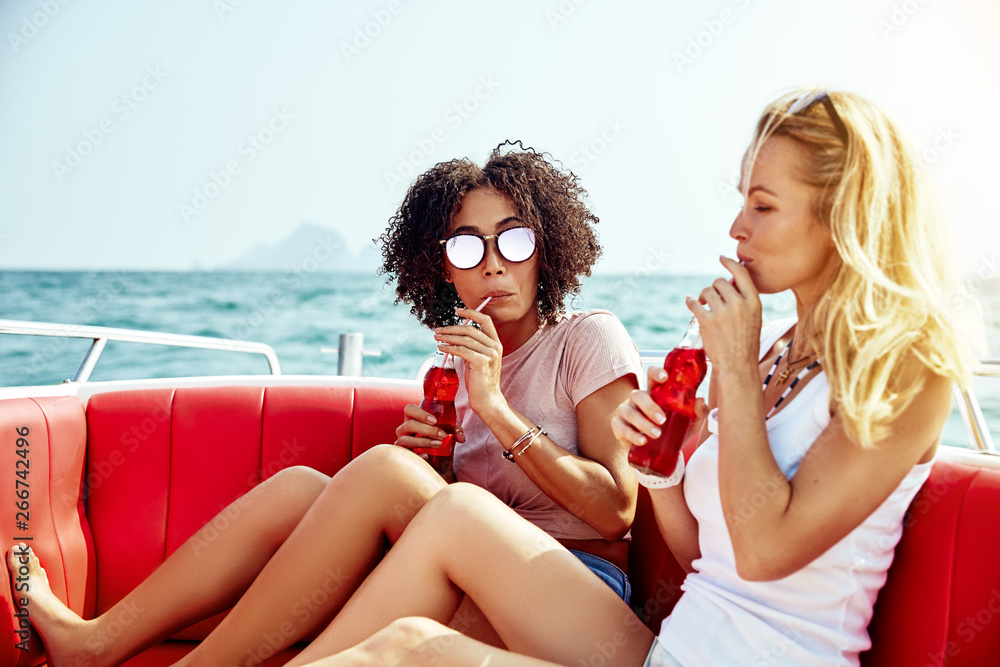 Two young friends relaxing on a boat with drinks