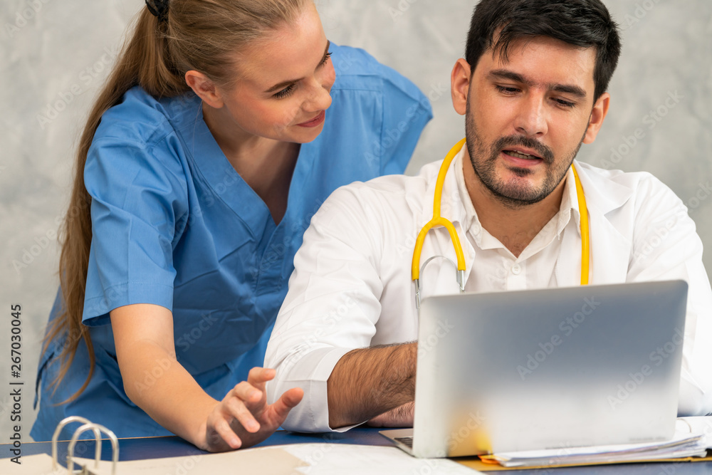 Happy doctor and nurse working with laptop computer in hospital office. Healthcare and medical conce