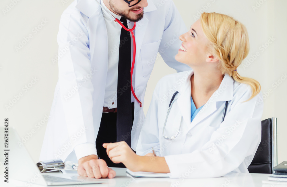 Doctor at hospital office writes notes on patients report while having conversation with another doc