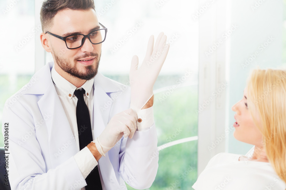 Young handsome dentist talks with happy woman patient sitting on dentist chair in dental clinic. Den