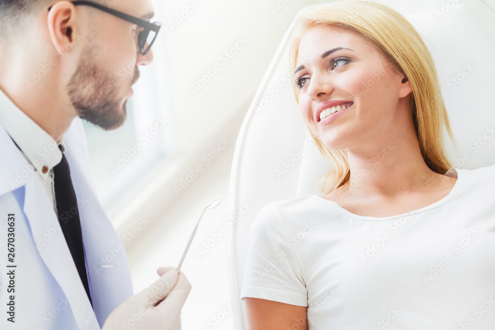 Young handsome dentist talks with happy woman patient sitting on dentist chair in dental clinic. Den