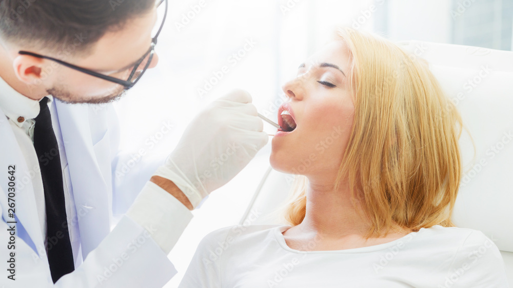 Young handsome dentist examining teeth of happy woman patient sitting on dentist chair in dental cli