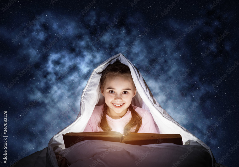 Happy little girl reading book in bed