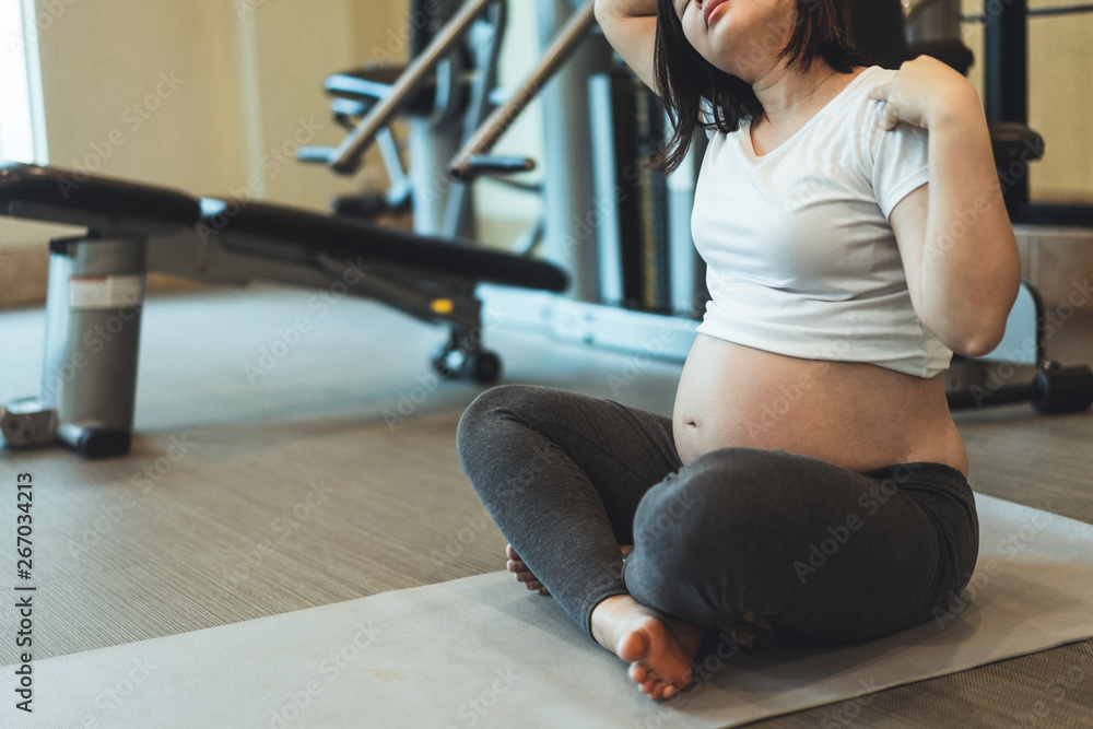 Active pregnant woman exercise in fitness center at yoga room. The young expecting mother holding ba