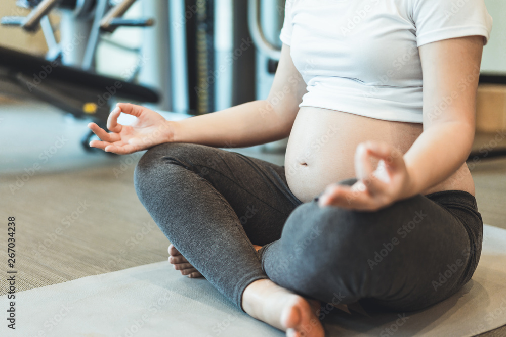 Active pregnant woman exercise in fitness center at yoga room. The young expecting mother holding ba