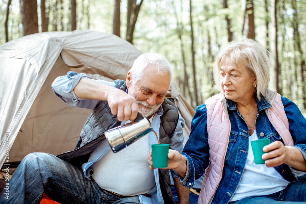 Senior couple pouring coffee having a picnic at the campsite in the forest