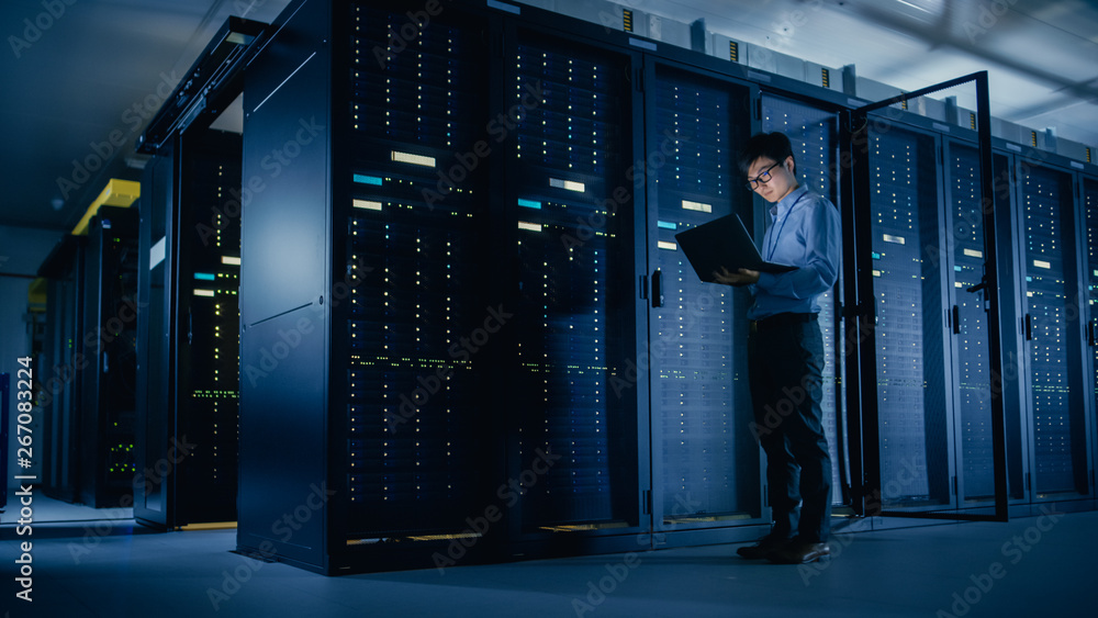 In Data Center: Male IT Technician Running Maintenance Programme on a Laptop, Controls Operational S