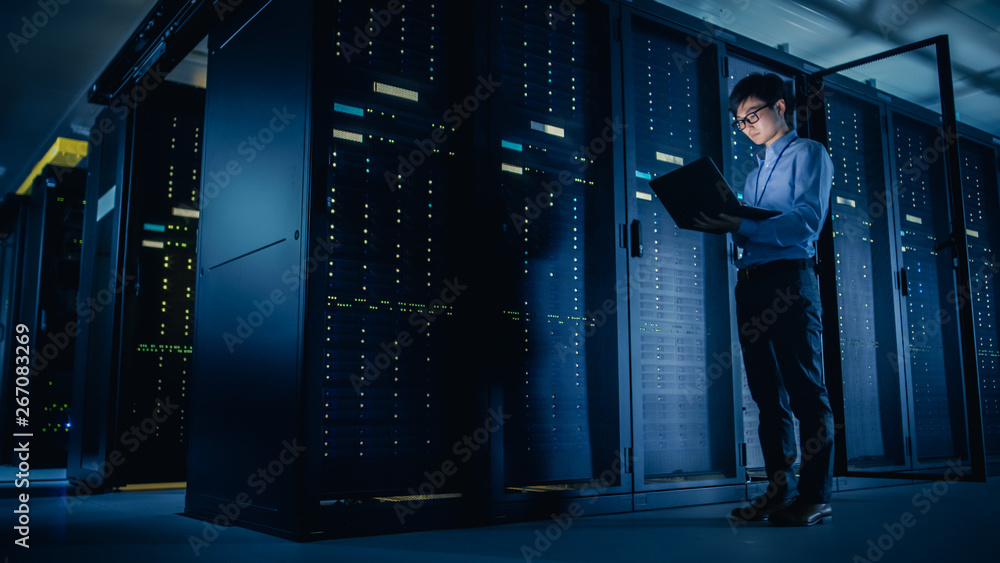 In Data Center: Male IT Technician Running Maintenance Programme on a Laptop, Controls Operational S