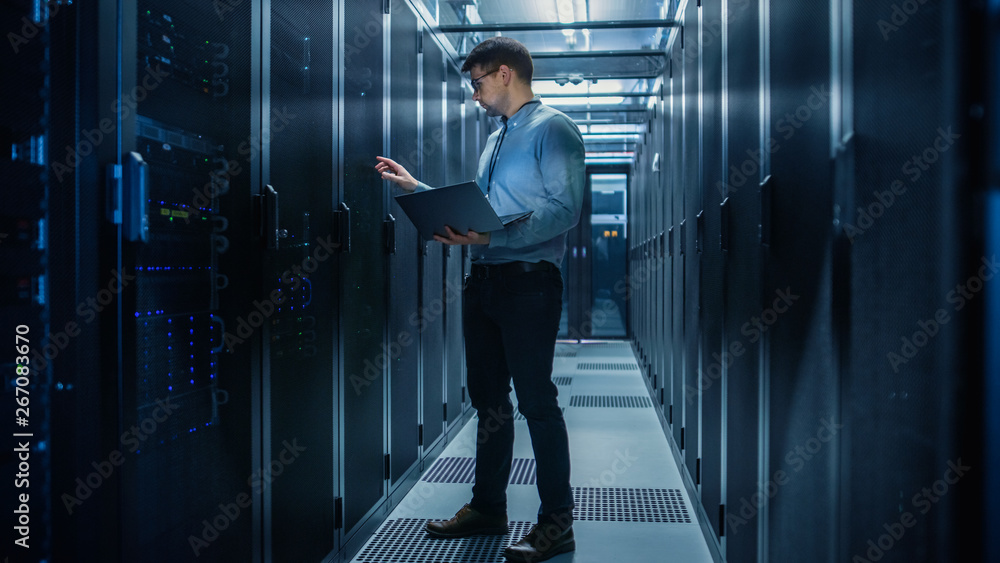 In Data Center IT Engineer Stands Before Working Server Rack Doing Routine Maintenance Check and Dia