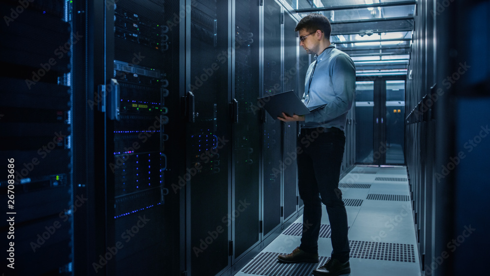 In Data Center IT Engineer Stands Before Working Server Rack Doing Routine Maintenance Check and Dia