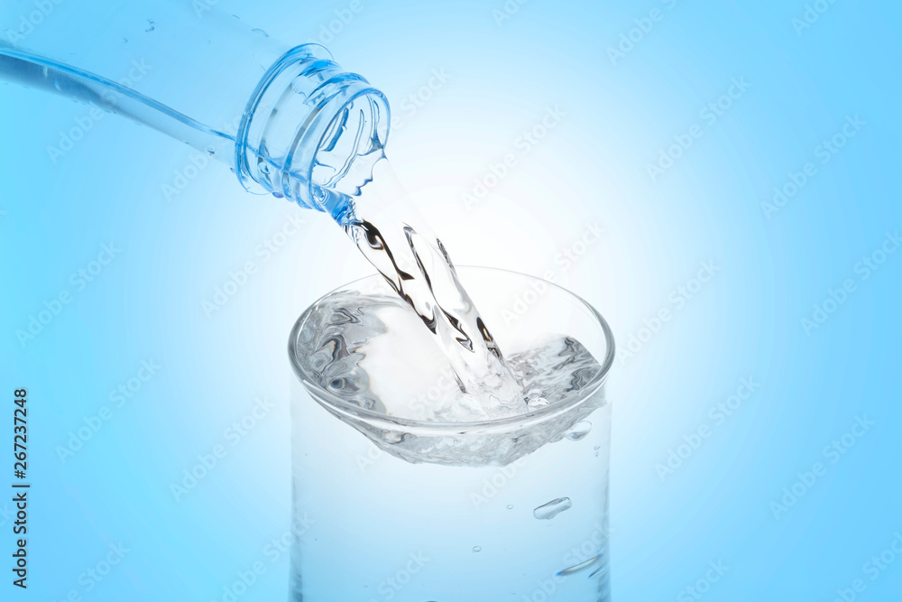 Pouring water from bottle into glass on blue background