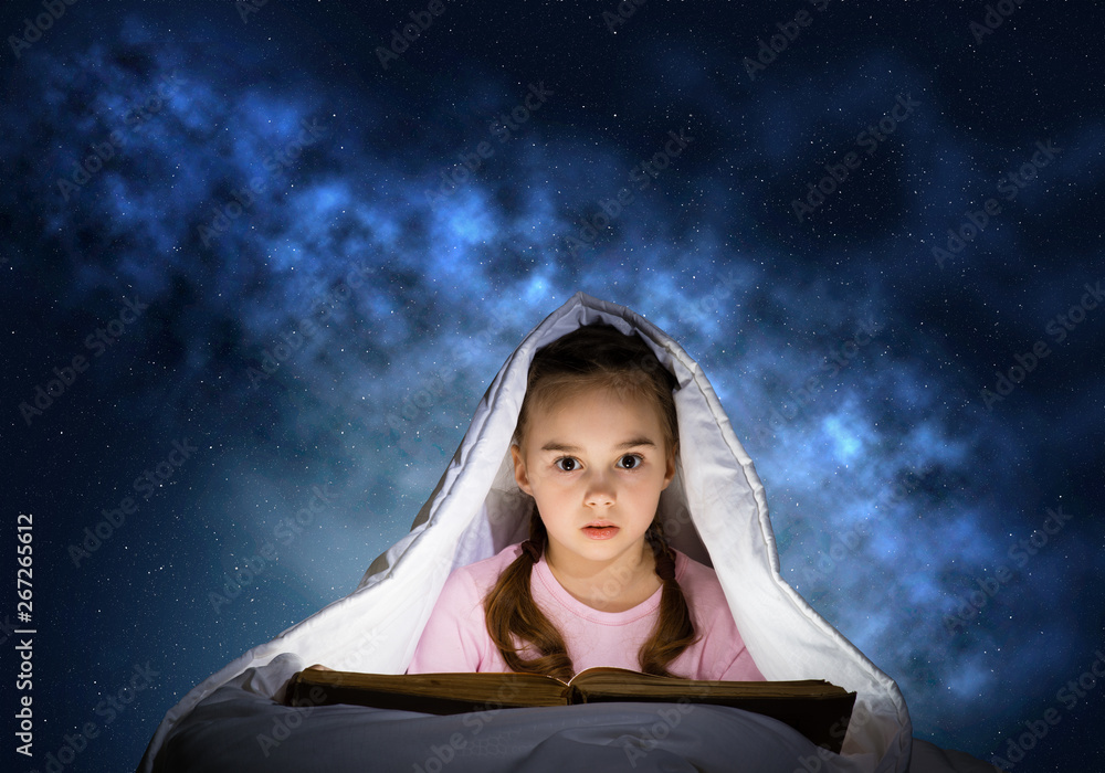 Little girl reading book in bed