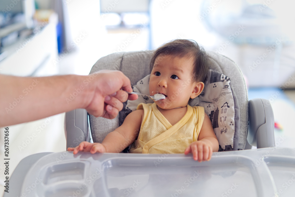 Father feeding porridge to his kid on baby feeding seat. The baby enjoy eating  meal and looking wit