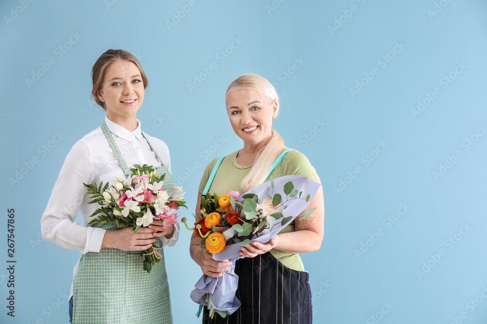 Female florists with bouquets on color background