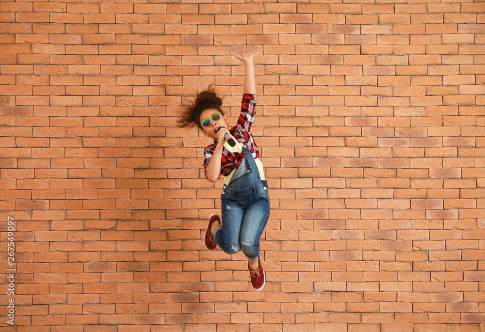 Jumping little African-American singer against brick wall