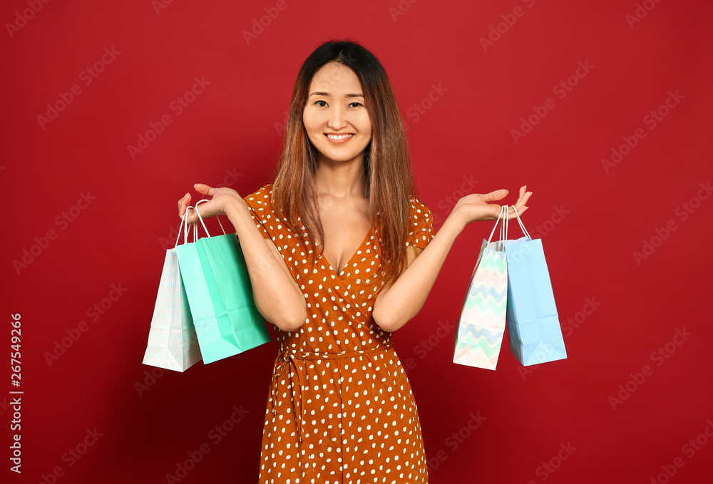 Asian woman with shopping bags on color background