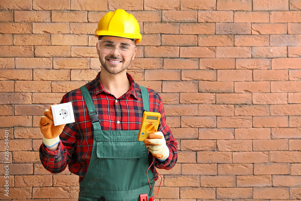 Male electrician with multimeter and socket near brick wall