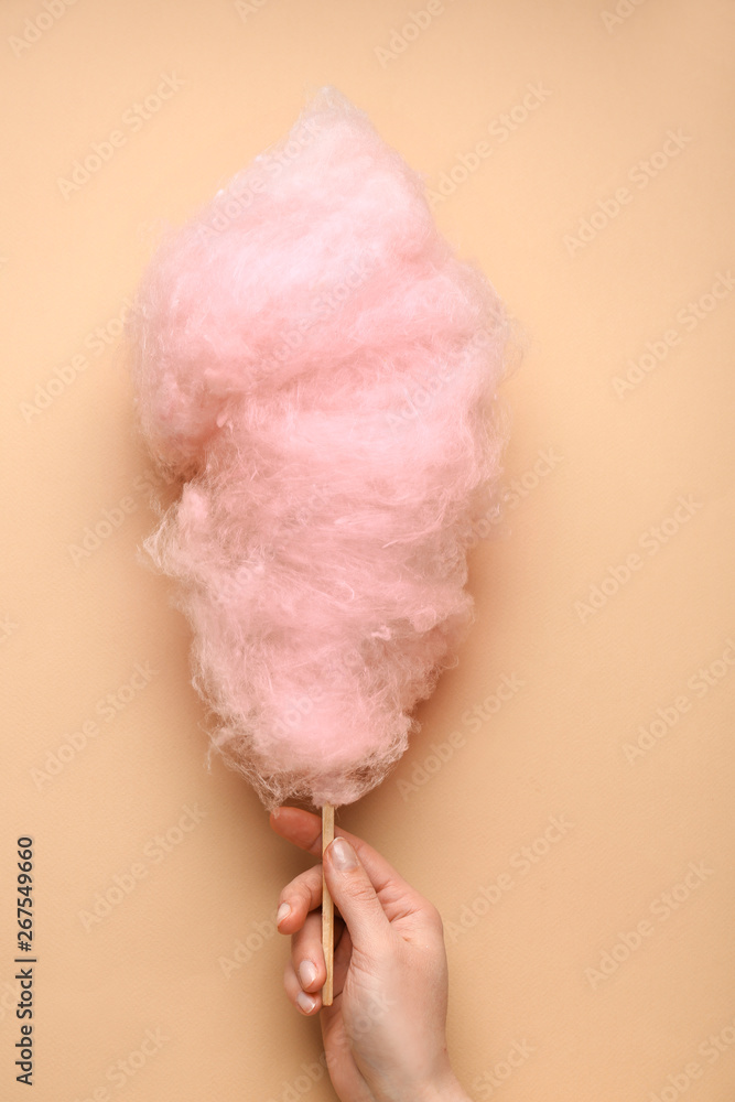 Female hand with tasty cotton candy on color background