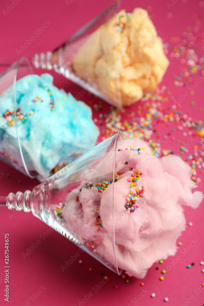 Glasses with tasty cotton candy and sprinkles on color background